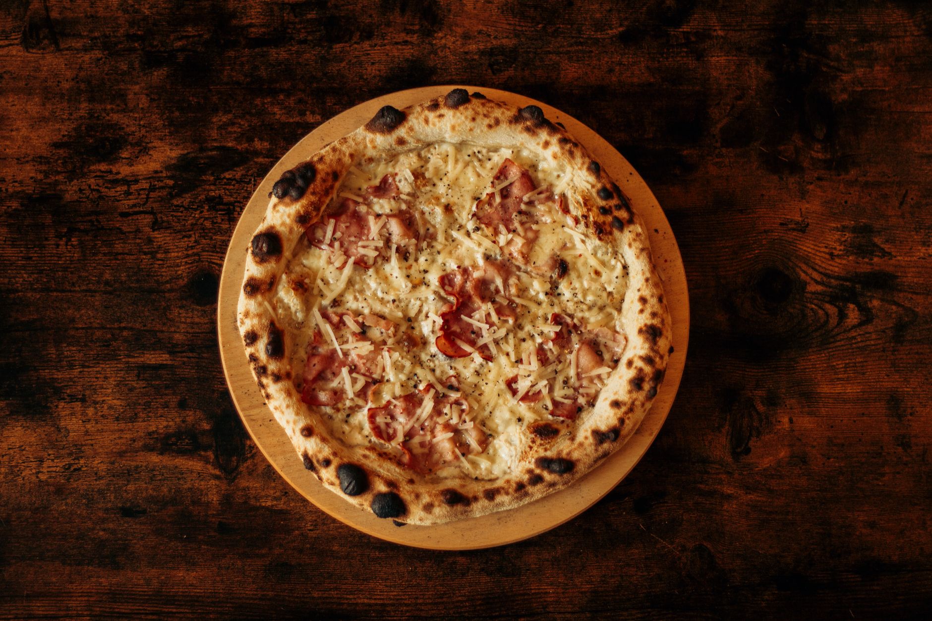 Koyu ahşap masada, ahşap tabakta benekli kenarlı Napoli pizzası — temsili görsel