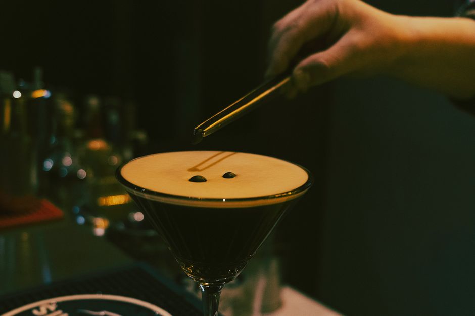 Barmen kokteyl hazırlıyor: cımbızla kadehin üstüne kahve çekirdeği koyuyor